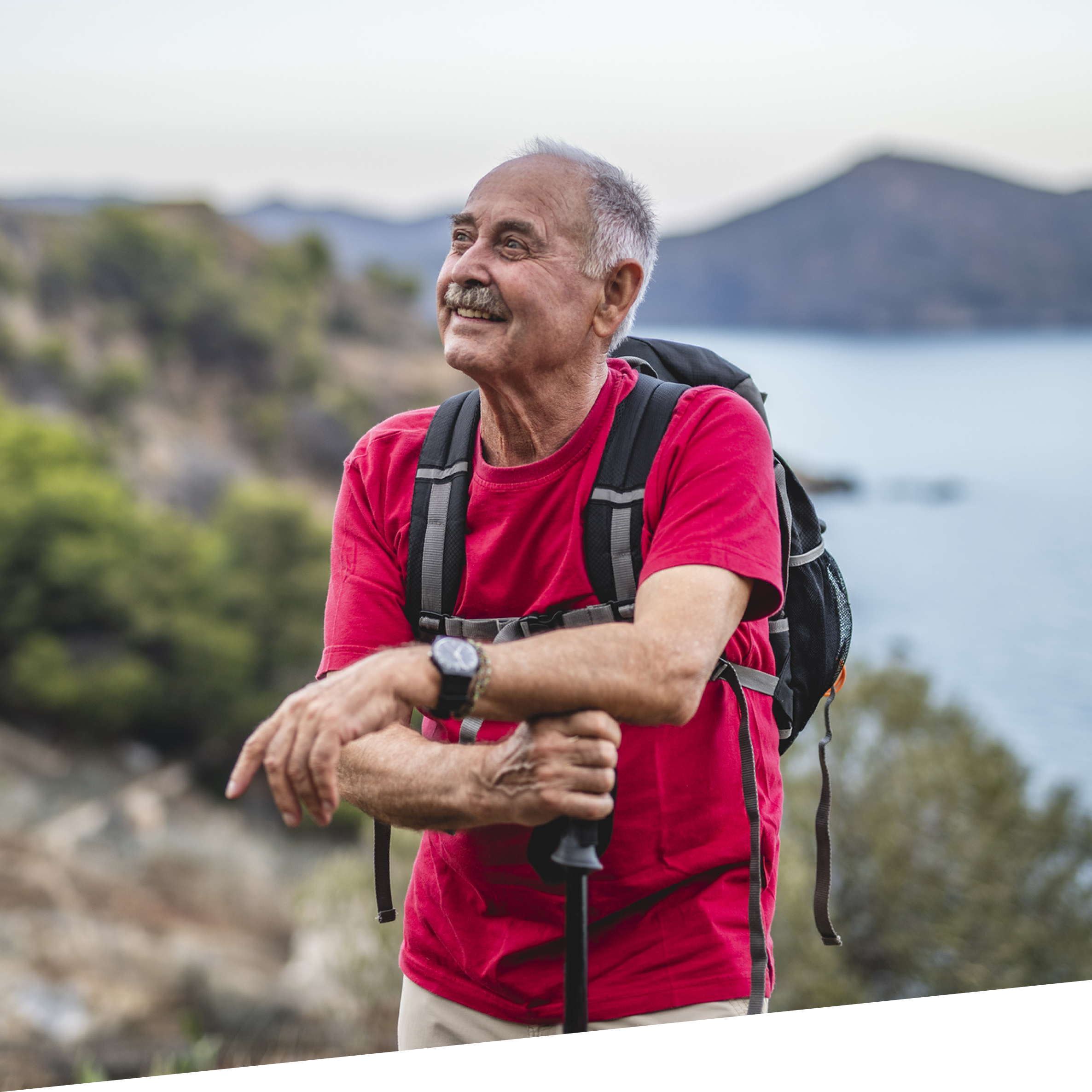 Older man rests during a hike, enjoying the mountain and lakefront scenery