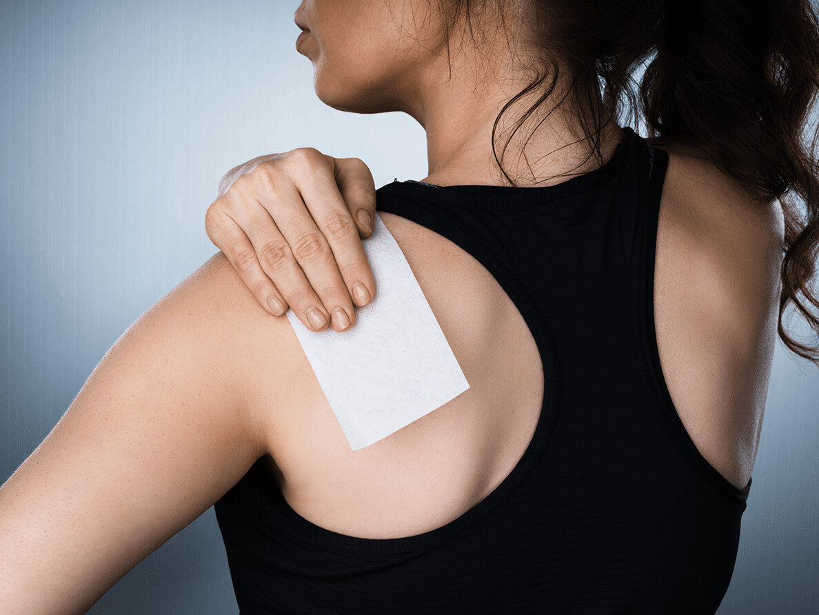 A woman applies a patch to her shoulder.