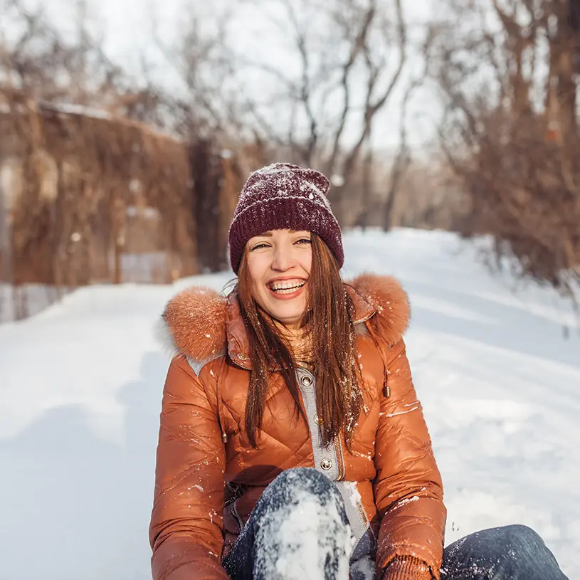 Una mujer sentada sobre la nieve riendo.