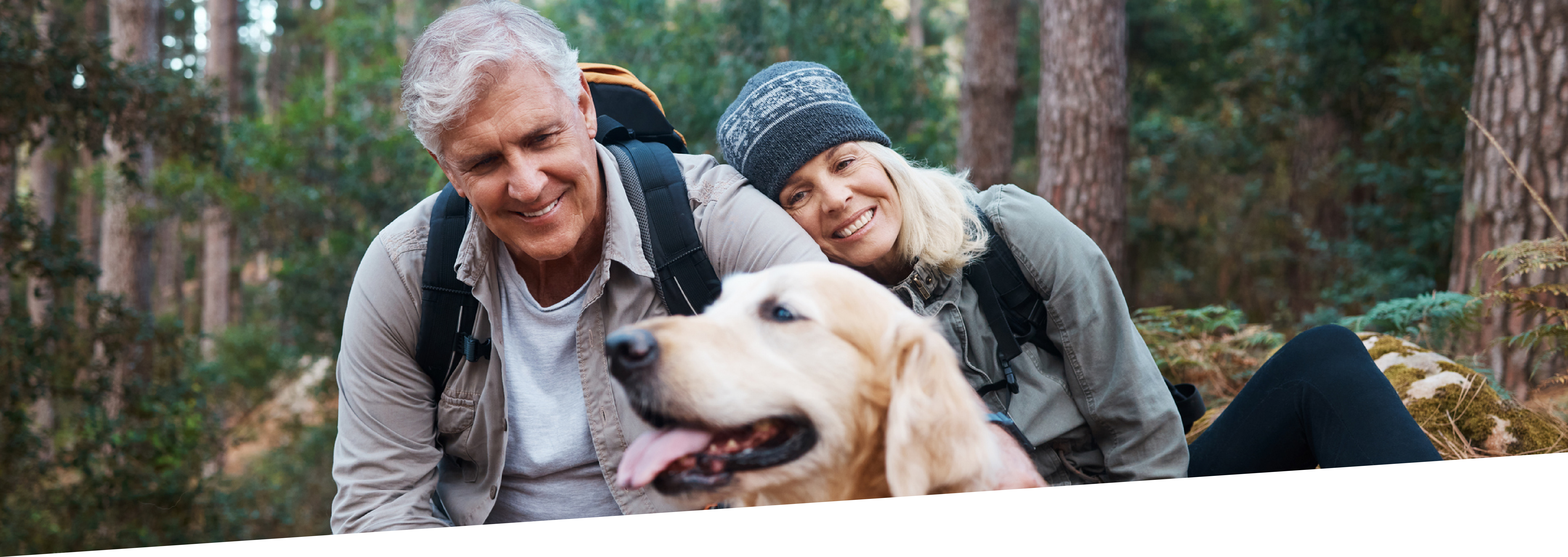 Middle-aged man and woman cuddle up with their golden retriever in the forest