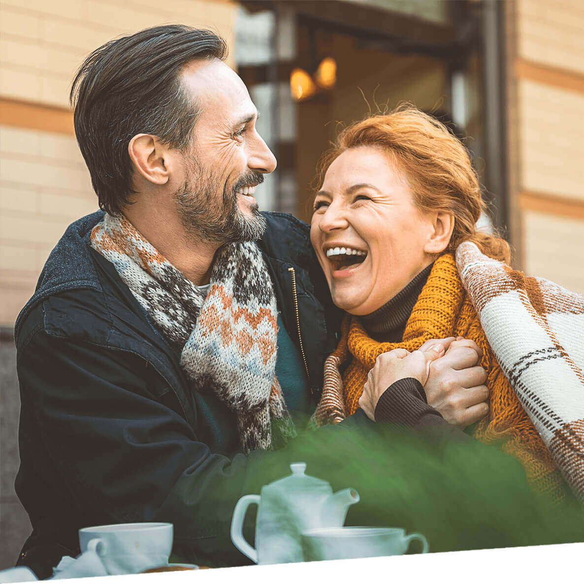 A couple laugh over cups of coffee.